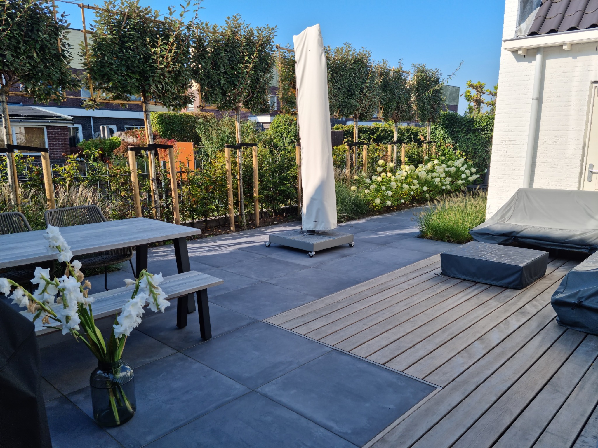 Aangelegde moderne achtertuin met groot terras, beplanting en vlonder
